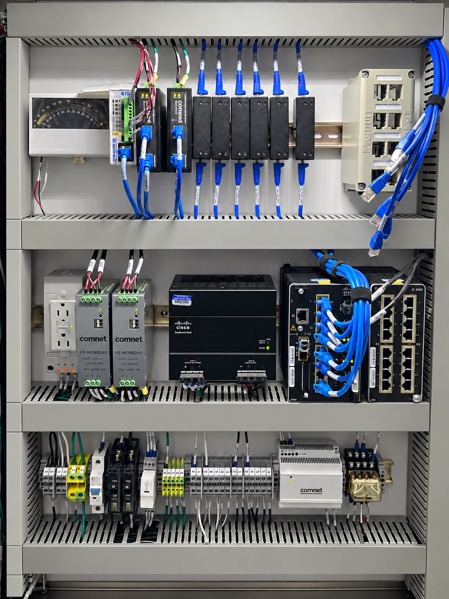 Communication cabinet with Cisco industrial network switches, Comnet power supplies, fiber media converters, labeled terminal blocks, and wire-duct covers